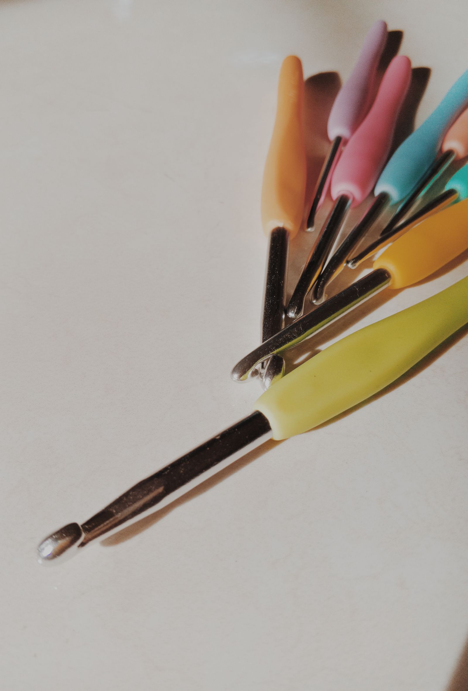 A set of colorful ergonomic crochet hooks arranged on a neutral surface