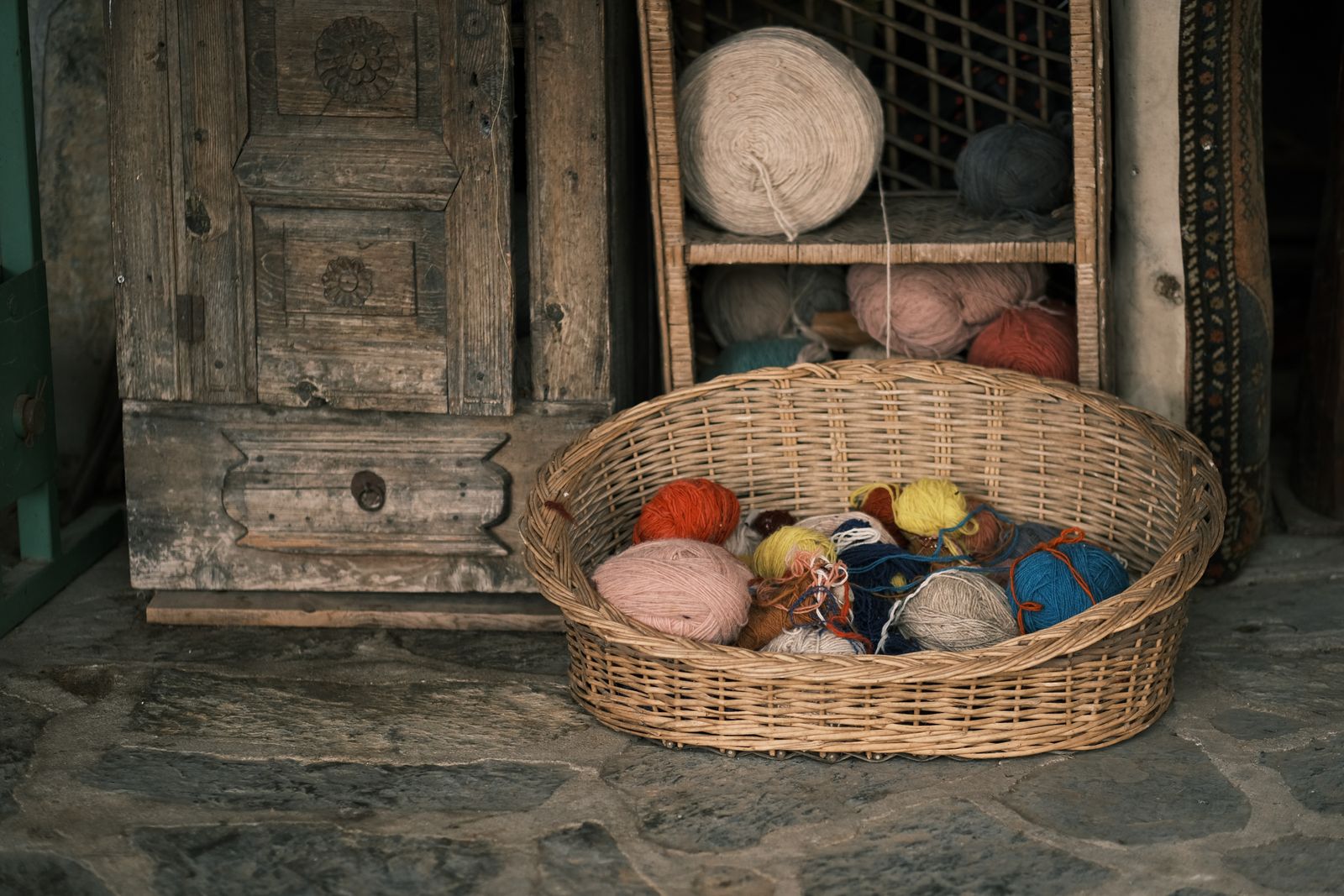Colorful yarn balls in a rustic wicker basket beside a wooden cabinet