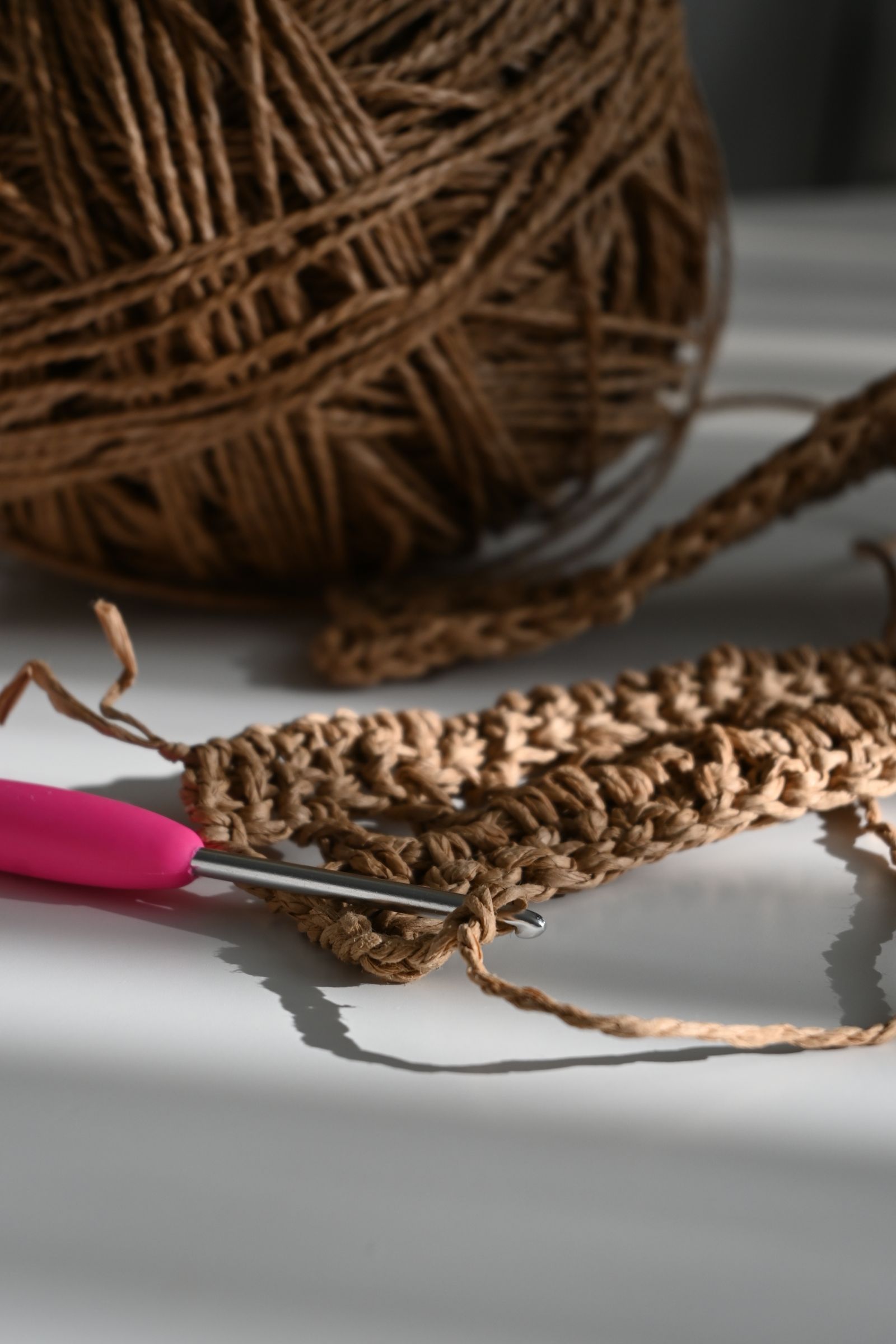 Crochet hook with yarn in progress on a sunny wooden table