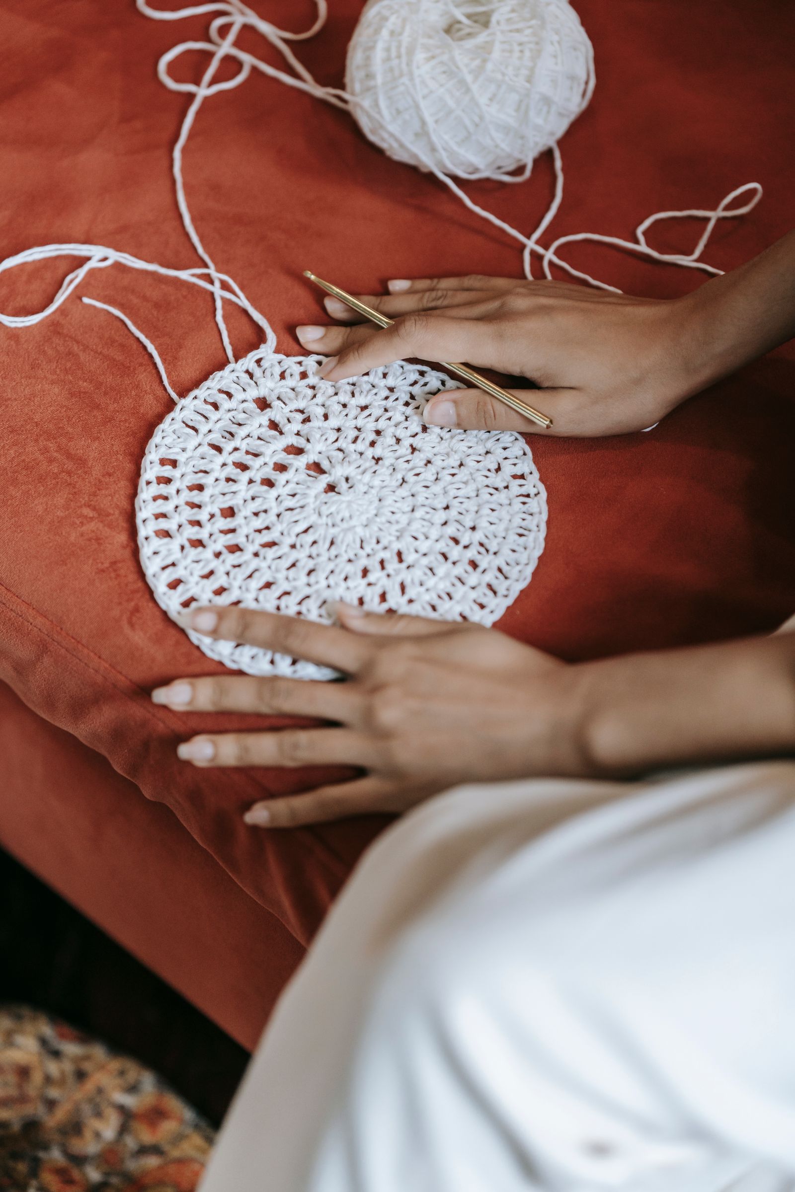 Hands with a round white crocheted piece on a warm surface
