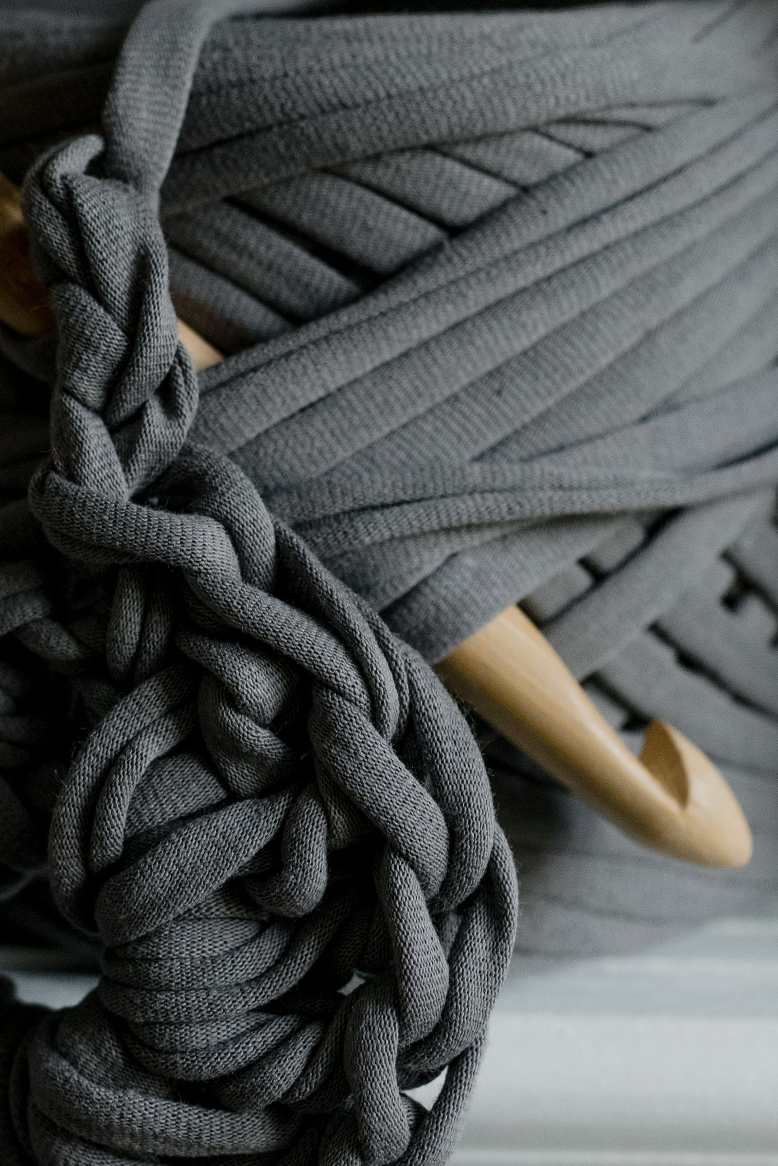 Detailed view of gray yarn with a wooden crochet hook