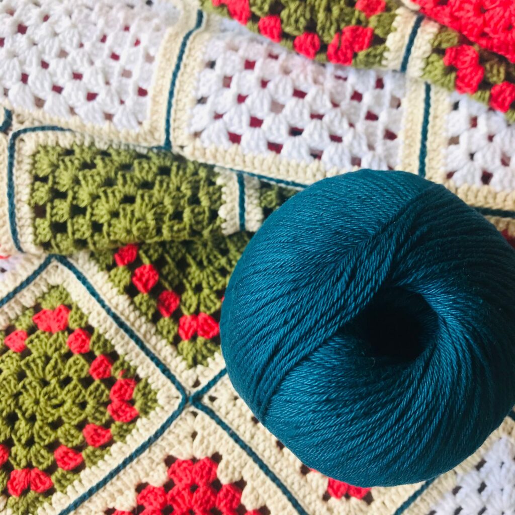 Close-up of a colorful crochet blanket with a teal yarn roll