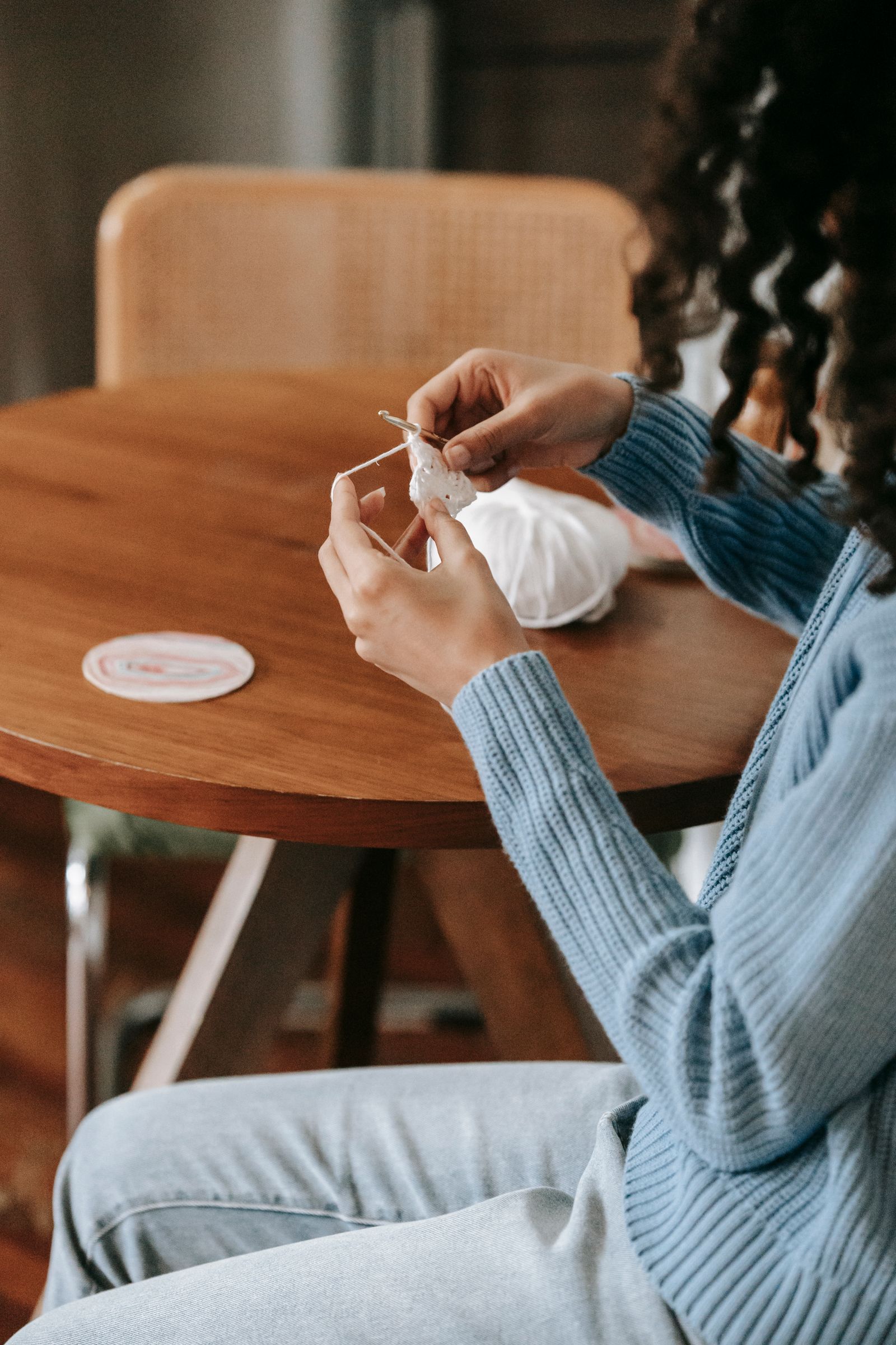 A woman sits at a wooden table crocheting, a tranquil indoor scene