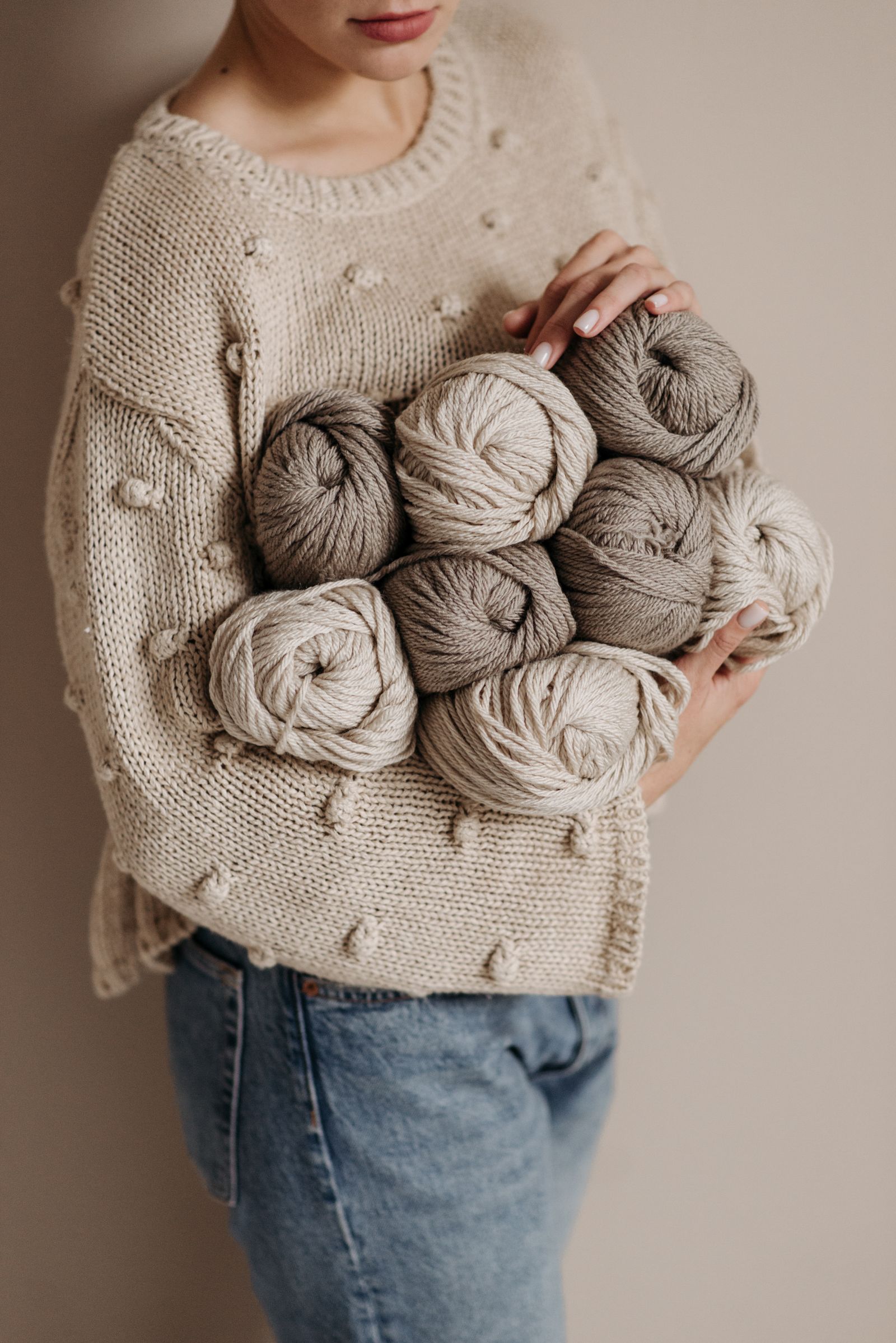 A person in a knitted sweater holding yarn balls, warm daylight